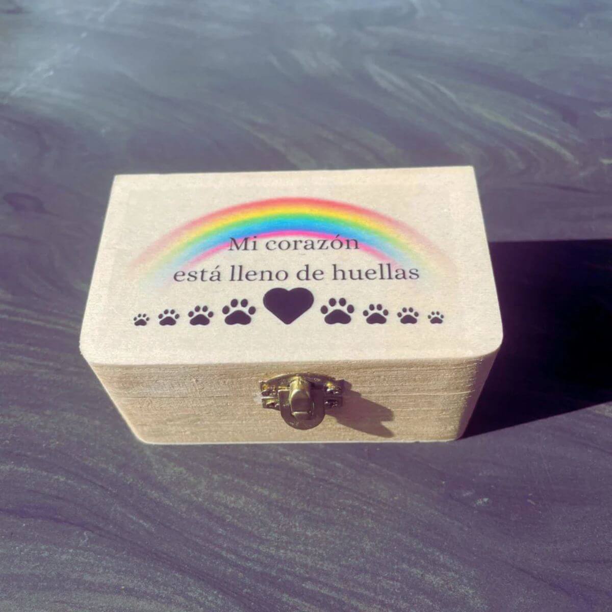 Caja de madera cerrada con tapa impresa “Mi corazón está lleno de huellas” y arcoíris, ideal para guardar el guijarro personalizado de tu mascota.
