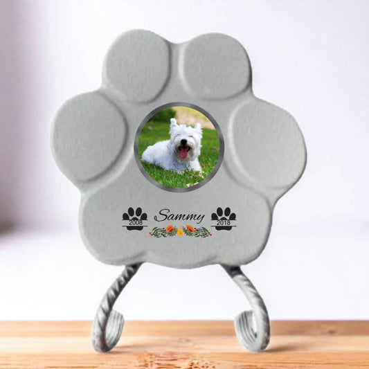 Lápida con forma de huella para mascotas, hecha de piedra gris, tamaño pequeño con soporte. Personalizada con foto, nombre y fechas importantes del perro o gato. Ejemplo de homenaje conmemorativo único.

