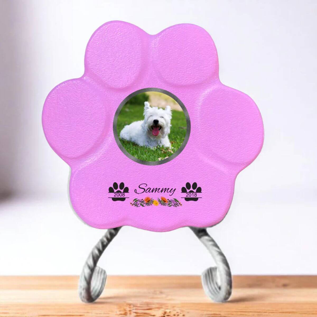 Lápida con forma de huella para mascotas, hecha de piedra rosa, tamaño pequeño con soporte. Personalizada con foto, nombre y fechas importantes del perro o gato. Ejemplo de homenaje conmemorativo único.

