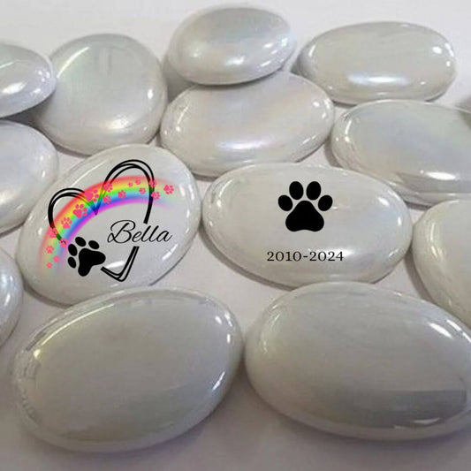 Guijarros de cristal blanco con diseño personalizado: uno con nombre Bella, arcoíris y huellas, y otro con huella negra y fechas. Conmemorativo para mascotas.