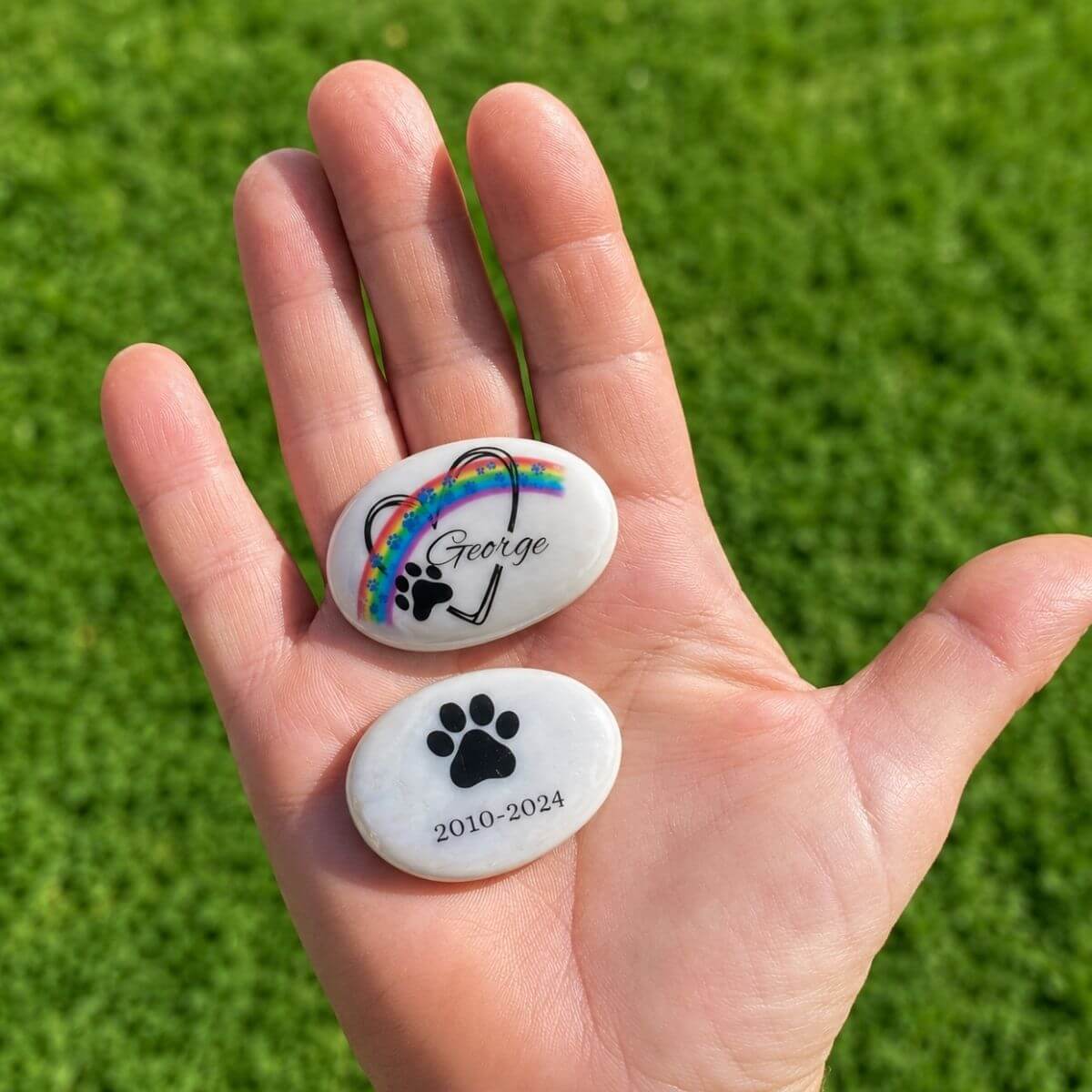 Guijarro de cristal personalizado para mascota con nombre George y reverso con huella y fechas de recuerdo, mostrado en la mano