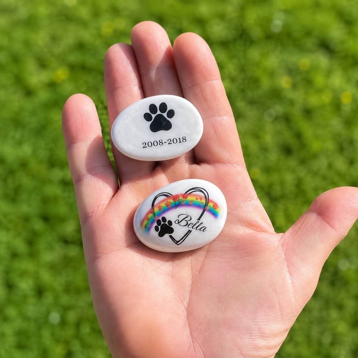 Guijarros de cristal personalizados para mascota con nombre Bella, diseño arcoíris, huella y fechas de recuerdo, mostrados en la mano