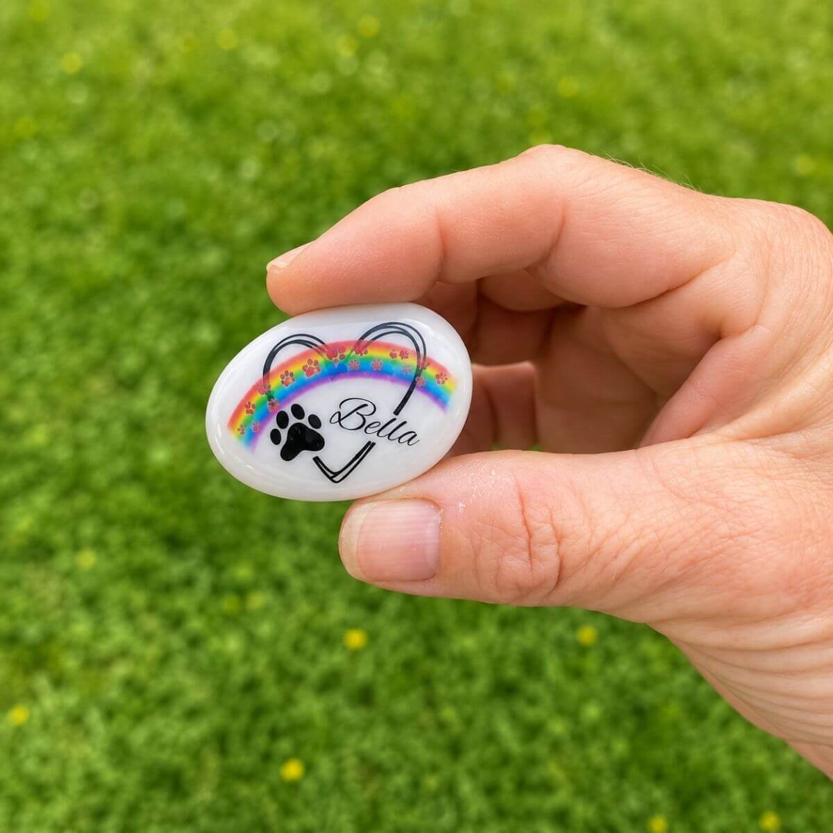 Guijarro de cristal personalizado para mascota con nombre Bella y huellas rosas, mostrado en la mano para apreciar su tamaño