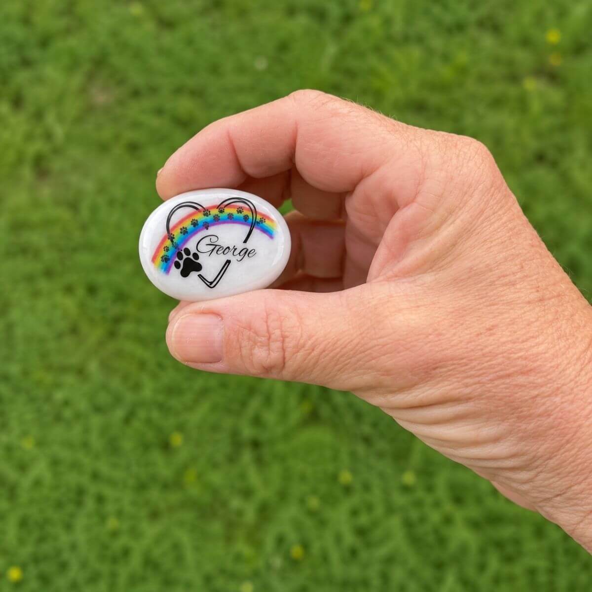 Guijarro de cristal personalizado para mascota con nombre George y huellas azules, mostrado en la mano para apreciar su tamaño