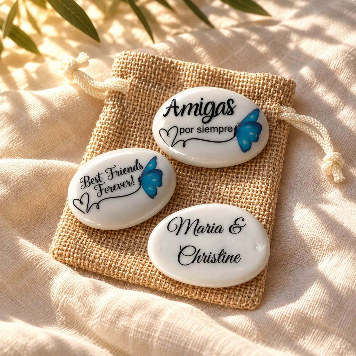 Piedra de amistad personalizada con mariposa azul, mensaje en español o inglés y nombres en el reverso, presentada sobre una bolsita de yute.