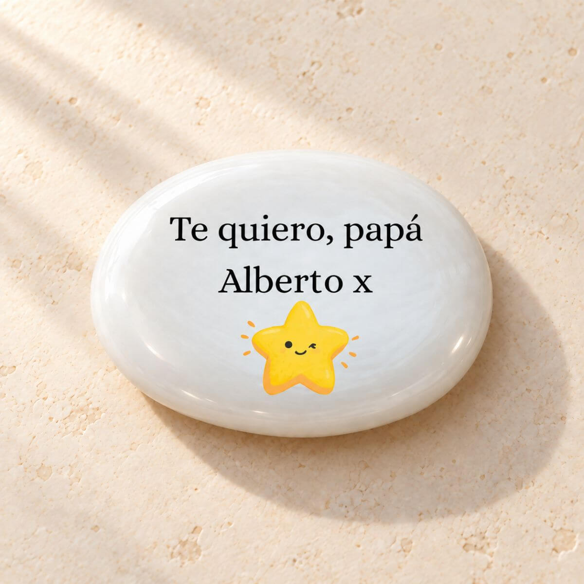 Reverso de piedra personalizada para papá con «Te quiero, papá», el nombre Alberto seguido de un beso «x» y una estrella amarilla sonriente sobre cristal blanco perlado.