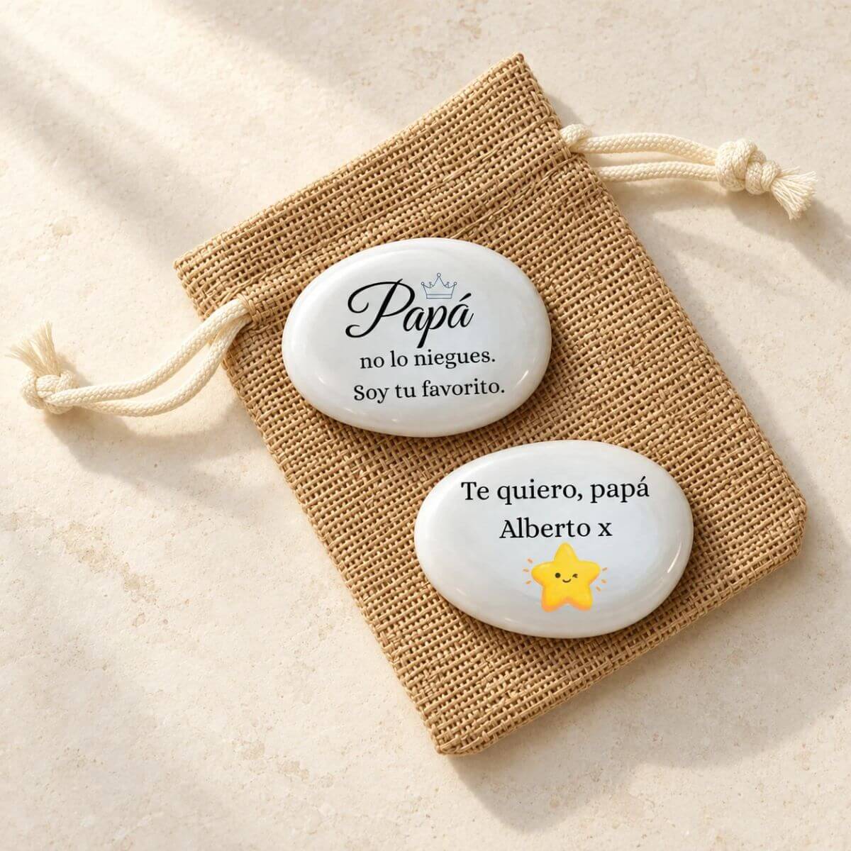 Piedra personalizada para papá con «Soy tu favorito» y corona azul; reverso con «Te quiero, papá», Alberto y estrella amarilla, sobre bolsita de yute.