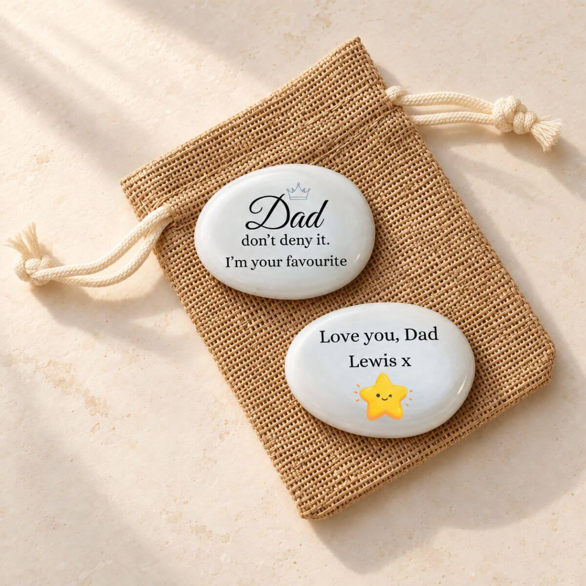 Piedra personalizada para papá en inglés con «I’m your favourite» y corona azul; reverso con «Love you, Dad», Lewis y estrella amarilla, sobre bolsita de yute.